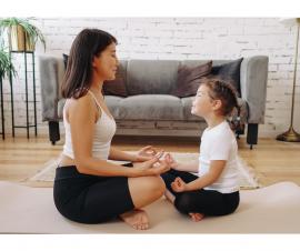 a female adult facing a female child sitting on the floor, eyes closed and legs cris-crossed