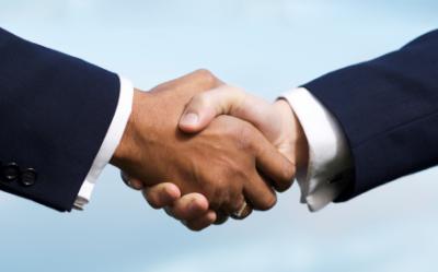Two people in business suits shake hands against a light blue background.