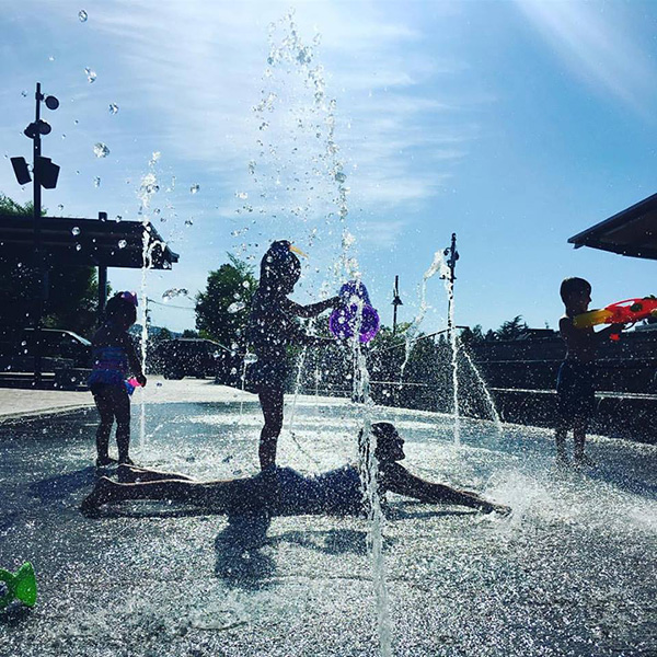 Children playing in a water fountain on a sunny day, silhouetted against the sky.