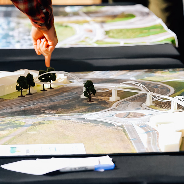 A person points at a 3D model of an infrastructure project with roads and bridges on a table.