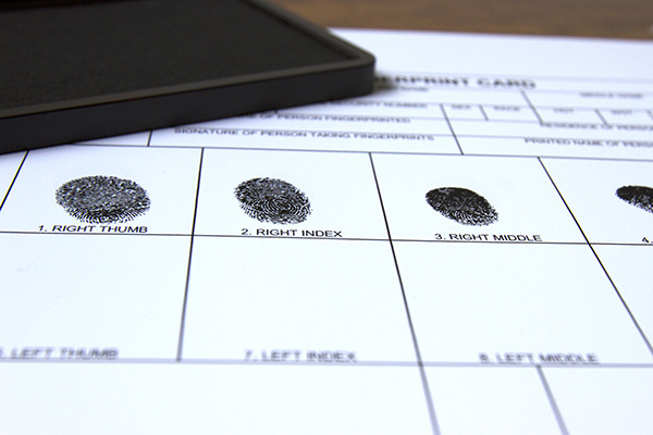 A fingerprint card with inked prints of right thumb, index, and middle fingers. A black ink pad is partially visible on the upper left.
