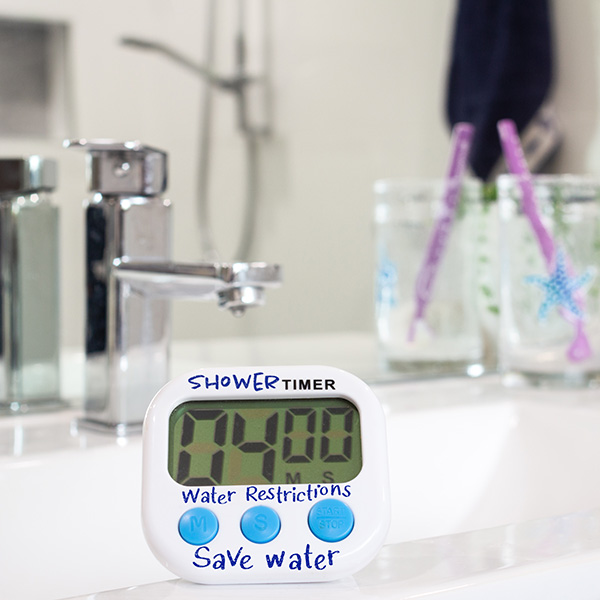 A shower timer on a bathroom sink displays 4:49. Nearby are two glasses with starfish designs, each holding a toothbrush.
