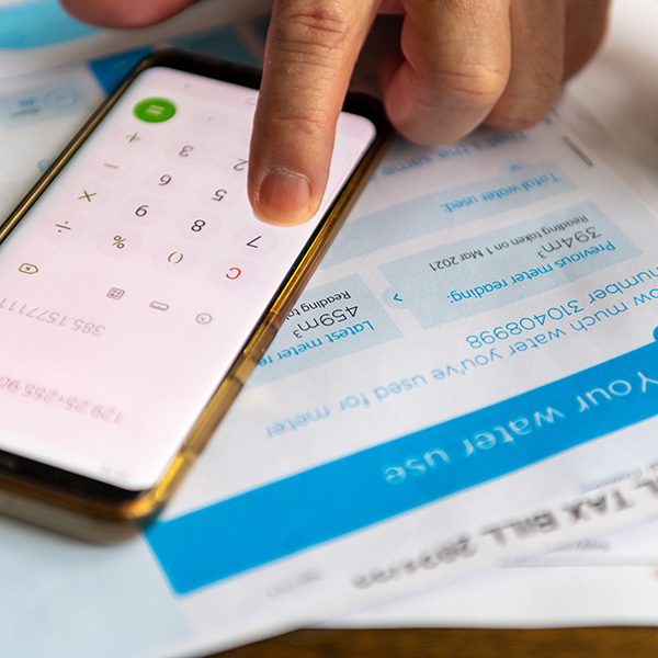 A hand uses a calculator app on a smartphone, positioned on top of utility bills.