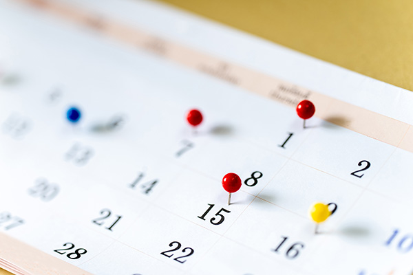 Close-up of a calendar page with red, blue, and yellow pushpins marking specific dates in a row.