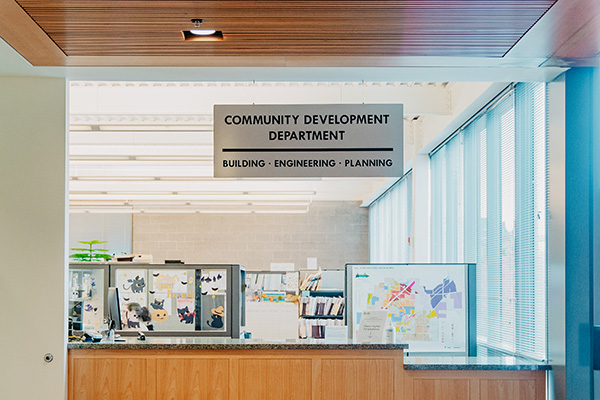 Interior of a Community Development Department office with a reception counter, office cubicles, and a sign above reading 