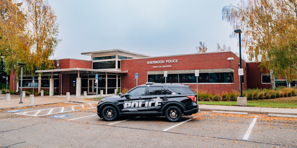 Police station with a patrol car parked in front, surrounded by autumn trees.