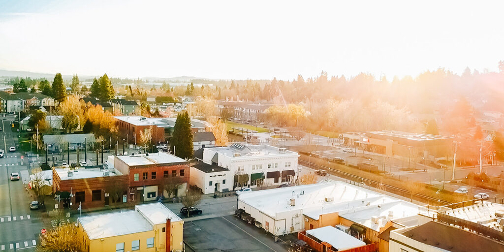 Aerial view of a small town with streets, buildings, and trees in the foreground, under a bright, hazy sky.