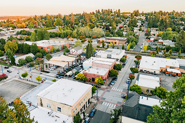 Aerial view of a small town with tree-lined streets, commercial buildings, and residential areas under a clear sky.