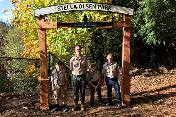 Four scouts in uniform stand under a wooden archway labeled 