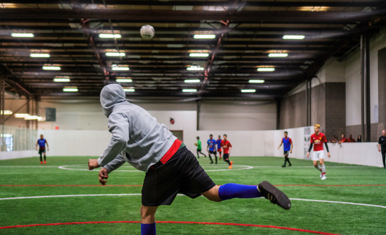A soccer goalie in a gray hoodie and black shorts throws the ball towards other team members on the field.