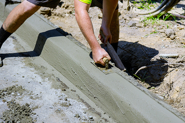 Worker smoothing wet concrete on a curb with a trowel outdoors.