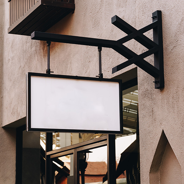 Blank rectangular sign mounted on a wall with a metal bracket above a glass storefront.