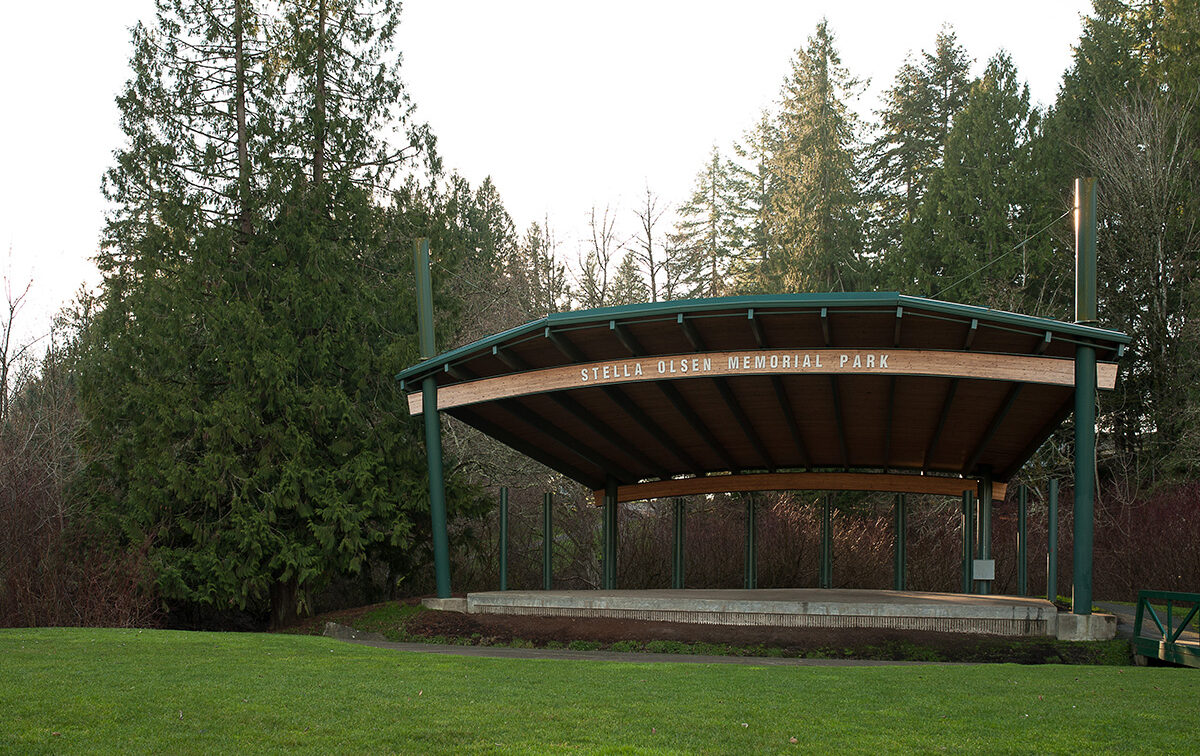 A wooden stage structure at Stella Olsen Memorial Park surrounded by trees and greenery.