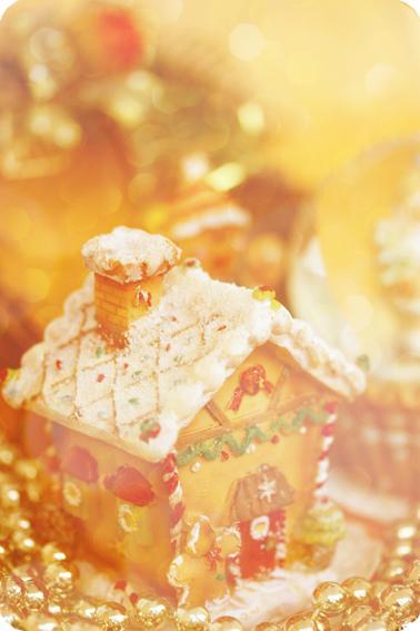 Gingerbread house with icing and candy decorations, set among golden ornaments, with a warm, blurry background.