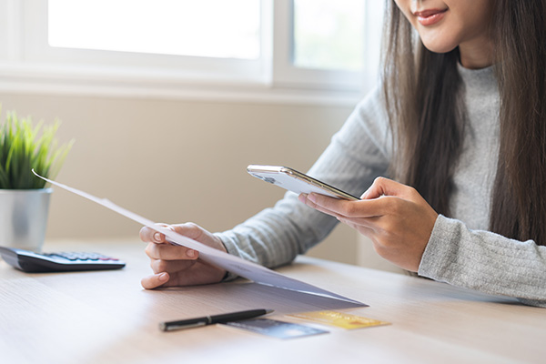 A young woman uses her phone to pay a bill.