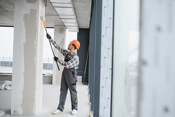 Professional builder using a paint roller, applying a fresh coat of paint to the walls of a building under renovation, demonstrating the process of interior finishing