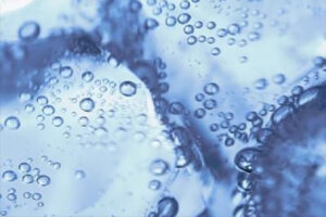Close-up of bubbles suspended in clear blue liquid, with ice cubes visible in the background.