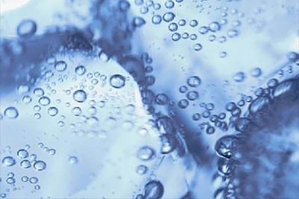 Close-up of bubbles suspended in clear blue liquid, with ice cubes visible in the background.
