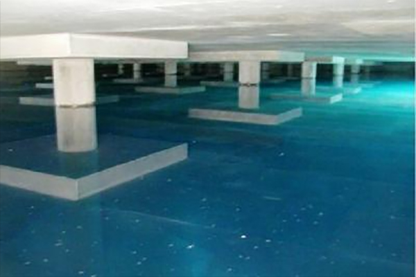Large, empty underground water storage tank with square concrete pillars and a shallow layer of clear blue water on the floor.