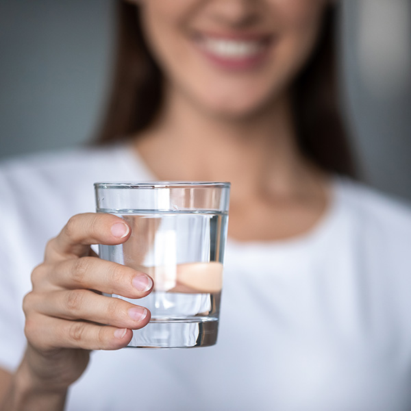 Smiling young lady holding fresh transparent pure filtered mineral water, happy healthy adult woman offering glass to camera as health care thirst hydration natural nutrition concept, close up view