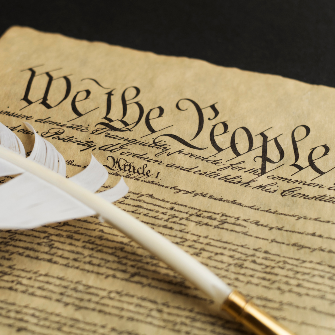 A close-up of the United States Constitution’s preamble, showing the words “We the People,” with a white quill pen resting on the document.