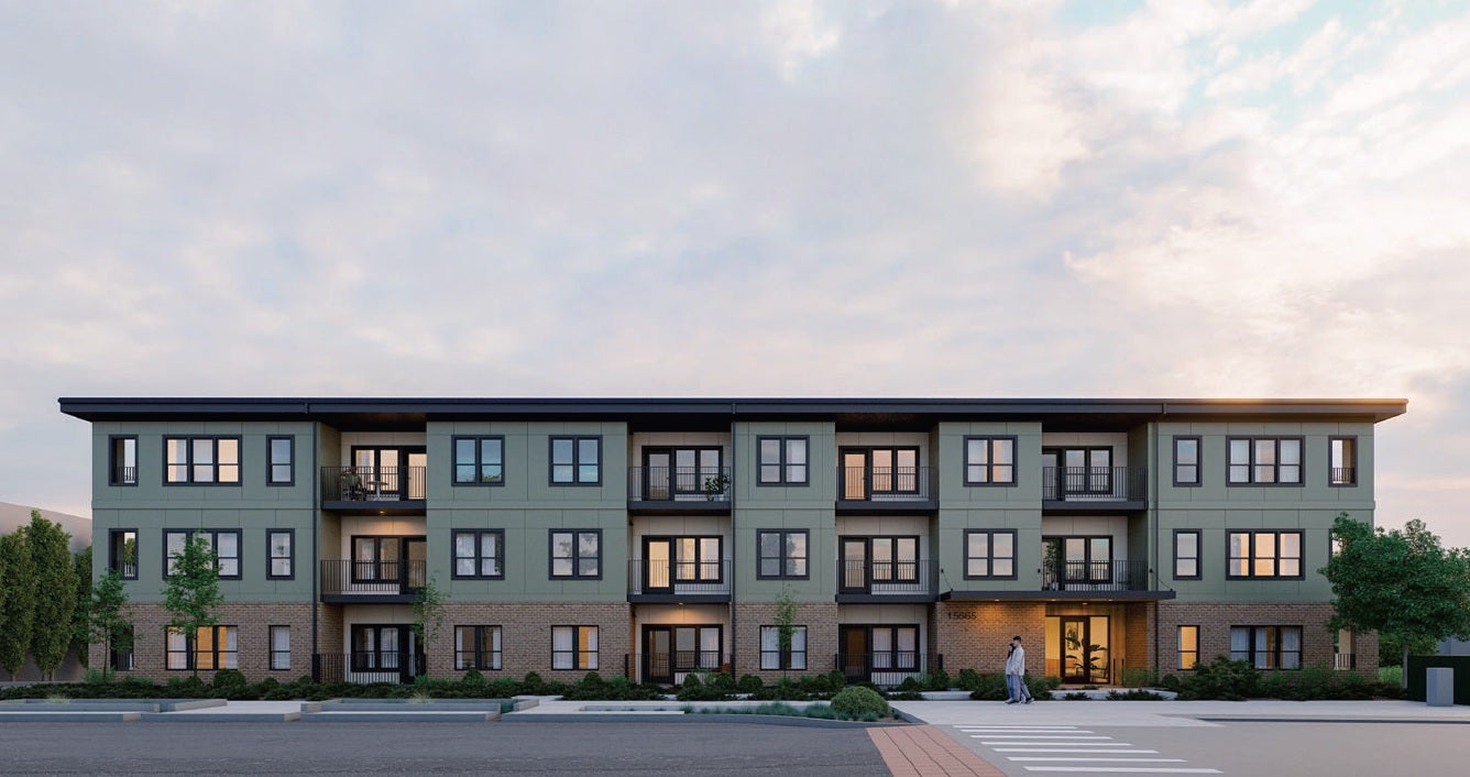 A modern three-story apartment building with green siding, large windows, balconies, and a brick ground floor, set against a cloudy sky. Two people are walking near the entrance.