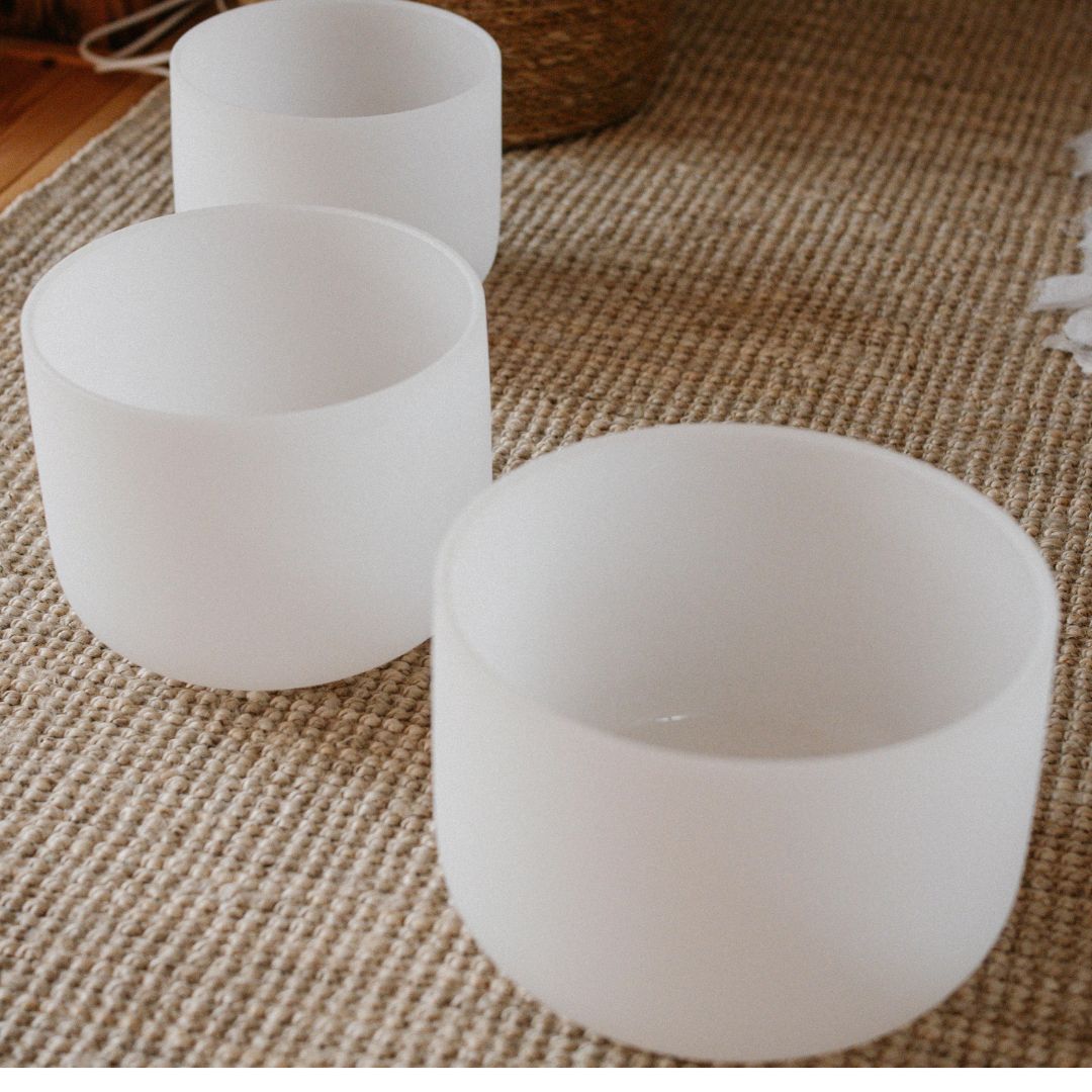 Three white frosted glass bowls sit on a textured beige rug, with part of a woven basket and white cords visible in the background.