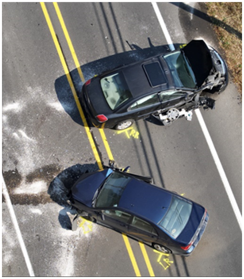 Aerial view of two dark-colored cars after a collision on a double yellow-lined road, with visible vehicle damage and debris on the pavement.