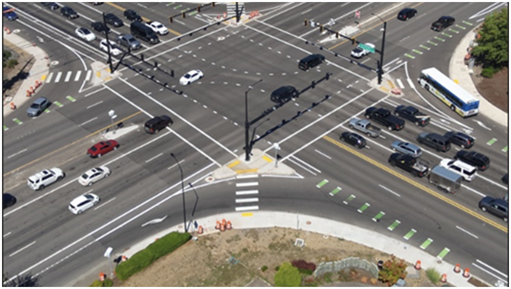 Aerial view of a large, busy multi-lane intersection with vehicles, bike lanes, crosswalks, and traffic signals visible.