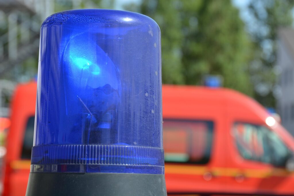 Close-up of a blue emergency vehicle siren light, with a blurred red emergency vehicle in the background.