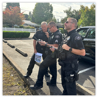 Three police officers stand in a parking lot, one holding a document, while the others look ahead and use handheld devices.