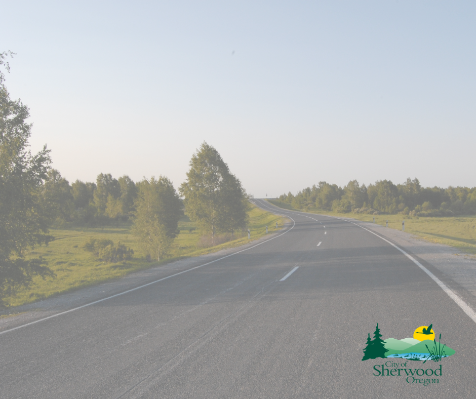 A paved road curves through a grassy, tree-lined landscape under a clear sky, with the City of Sherwood, Oregon logo in the lower right corner.