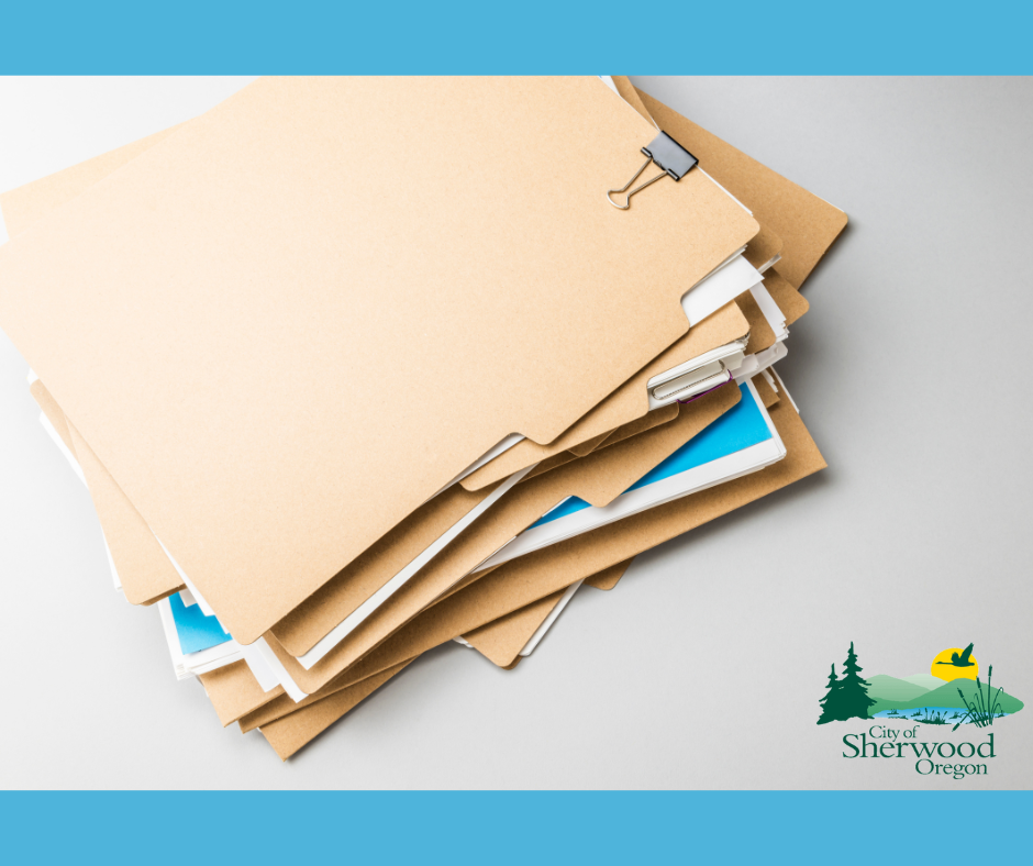 A stack of manila file folders is arranged on a white surface, with a binder clip on top. The City of Sherwood, Oregon logo appears in the bottom right corner.