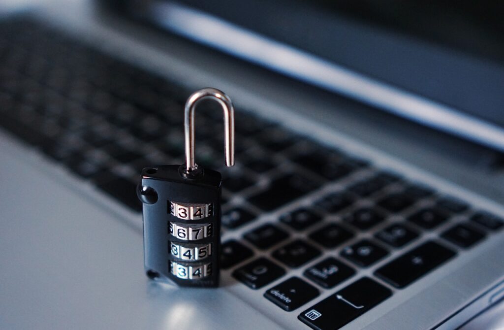 A combination padlock with an open shackle rests on a laptop keyboard.