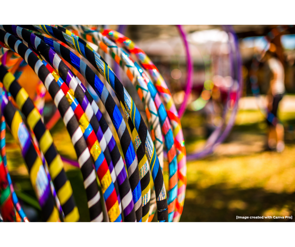 Colorful hula hoops arranged in rows are displayed outdoors, with a blurred background of grass, sunlight, and indistinct people.