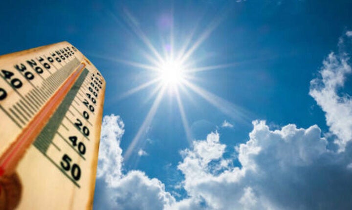 A thermometer shows high temperatures under a bright sun in a blue sky with scattered clouds.