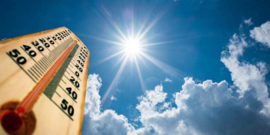 A thermometer shows high temperatures under a bright sun in a blue sky with scattered clouds.