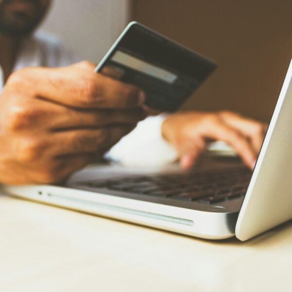 A person holding a credit card in one hand and typing on a laptop with the other, suggesting an online payment.
