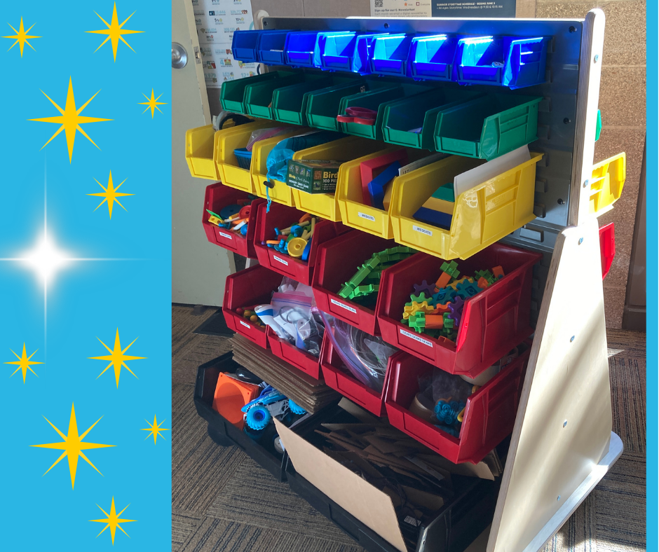 Storage rack with blue, green, yellow, and red bins holding various small toys and parts, positioned indoors next to a wall and a door. A blue starburst design borders the left side.