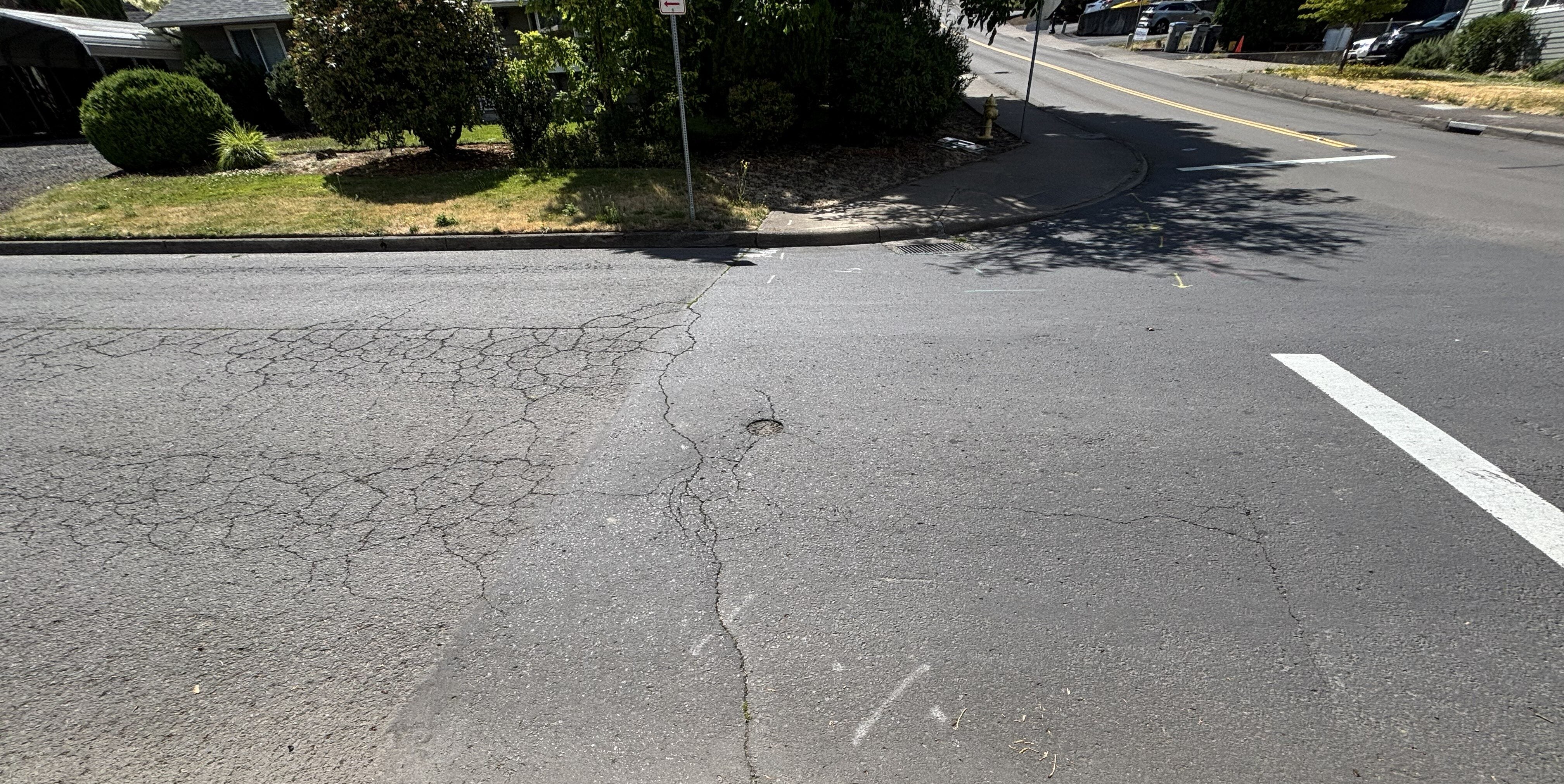 An asphalt road intersection with a cracked surface and white lane markings.