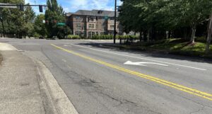 An asphalt intersection showing a left-turn lane, double yellow lines, and a multi-story building in the background.