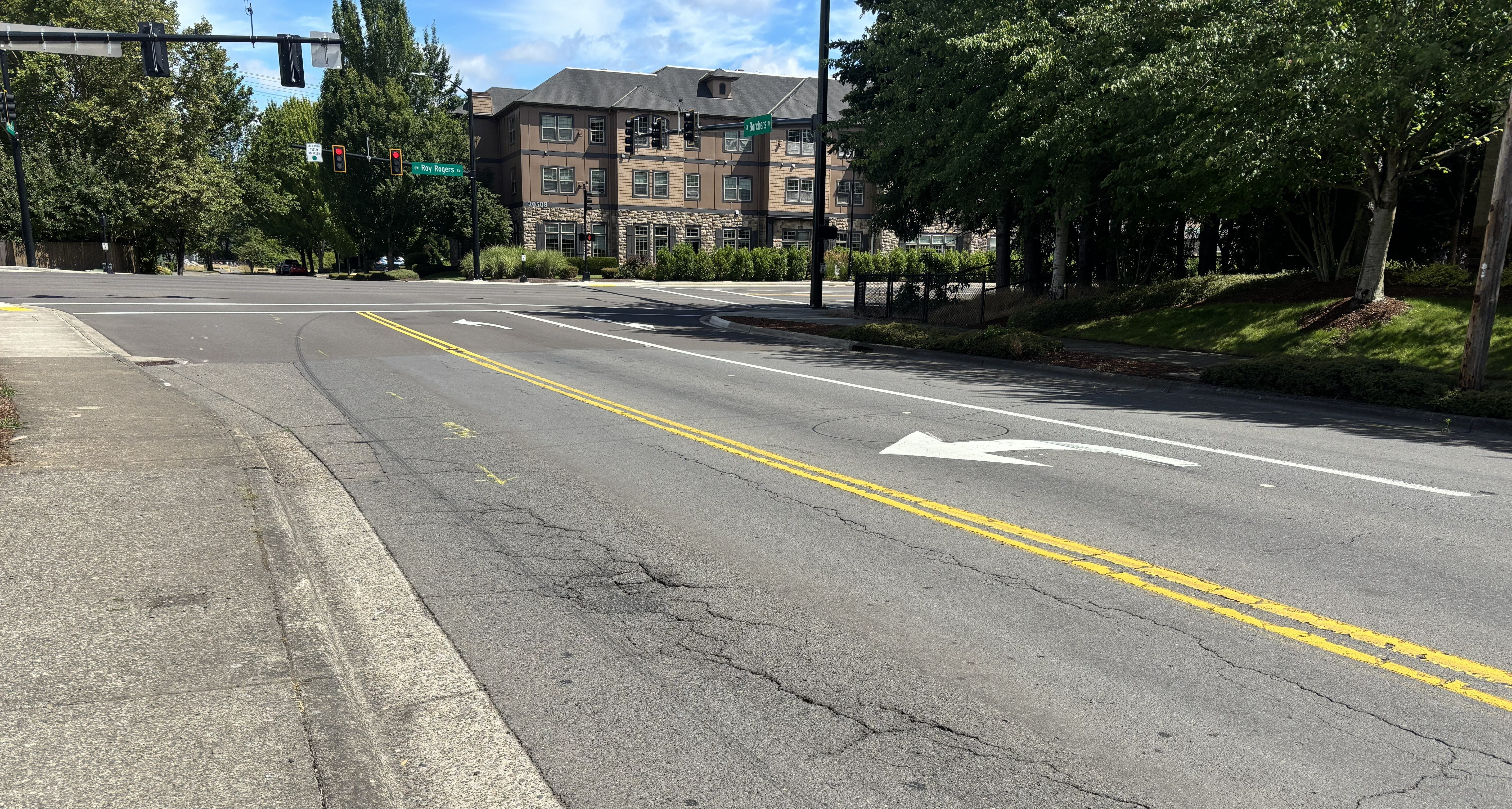 An asphalt intersection showing a left-turn lane, double yellow lines, and a multi-story building in the background.