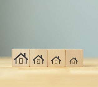 Four wooden blocks in a row, each featuring an icon of a house that decreases in size from left to right.