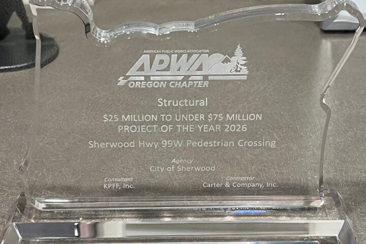 Clear acrylic award in the shape of Oregon, engraved with “APWA Oregon Chapter,” project details for the Sherwood Hwy 99W Pedestrian Crossing, and names of the agency, consultant, and contractor.