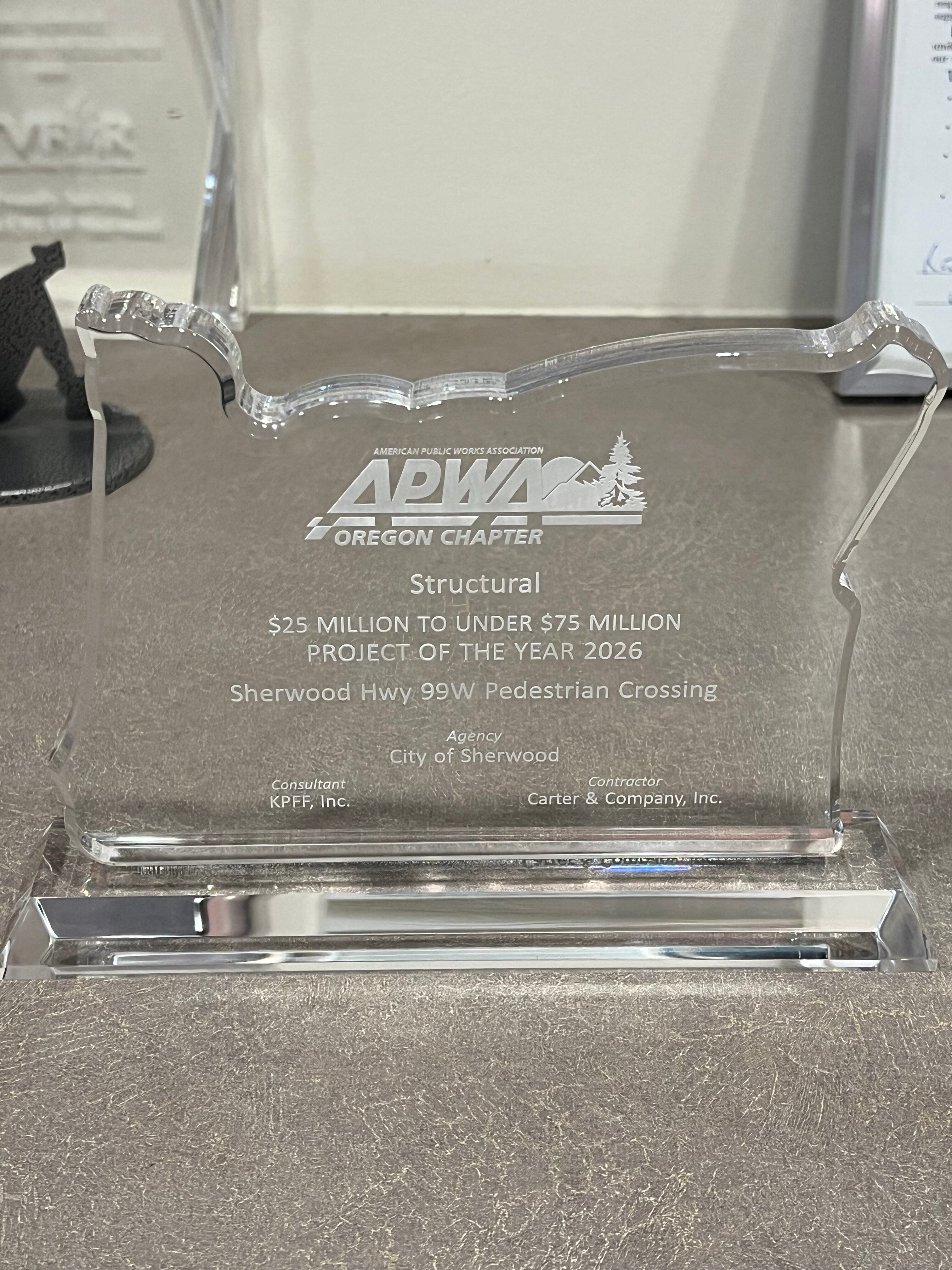 Clear acrylic award in the shape of Oregon, engraved with “APWA Oregon Chapter,” project details for the Sherwood Hwy 99W Pedestrian Crossing, and names of the agency, consultant, and contractor.